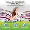 A young woman is tucked into a bed with striped bedding, covering her face with a pillow. The image is framed by a green gradient at the bottom, featuring icons and text highlighting product features. Produktbild-Vorschau