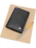 A black Lacoste wallet and a pen are placed on a brown notebook. Anteprima dell’immagine prodotto