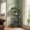 A multi-tiered metal plant stand with heart-shaped shelves filled with various potted plants, placed in a well-lit room near a window. Náhled obrázku produktu