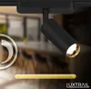A close-up view of a black track light fixture, with a blurred background of a dining area. Produktbild-Vorschau