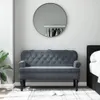 A dark gray velvet bench with a tufted backrest is placed in a room with a round mirror on the wall and a bed on the right. Náhled obrázku produktu
