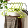 Several plastic clothes hangers with clothes on them are hanging on a clothes rack. A plant is visible in the background. Anteprima dell’immagine prodotto