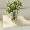 A vase of white flowers sits on a light-colored surface, casting a shadow. Voir les images du produit