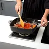 A person is cooking in a kitchen, stirring food in a square pan on a stovetop. Náhled obrázku produktu