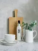 A still life arrangement of kitchenware and a bottle of liquid on a marble countertop against a textured gray wall. Produktbild-Vorschau