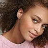 Close-up of a woman's face and shoulder wearing earrings and a pink sweater. Produktbild-Vorschau