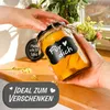 Hands holding a jar of preserved fruit, with a decorative label. Produktbild-Vorschau