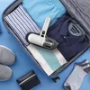 A handheld vacuum cleaner is placed on top of folded clothes inside an open suitcase, with shoes and a wallet nearby. Voir les images du produit