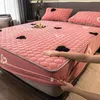 A person's hands are shown adjusting a pink bedsheet with heart patterns on a bed. The bed is made with matching pillows and a small tray with items on it. Náhled obrázku produktu