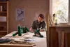 A man is working on a table with various tools, including a heat gun and glue guns. Produktbild-Vorschau
