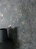 A close-up shot of a textured wall with gold accents and a black vase in the foreground. Produktbild-Vorschau