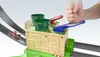 A child's hand is shown pressing a blue lever on a toy race track. Produktbild-Vorschau