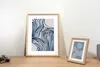 Two framed pictures with abstract art are displayed on a wooden surface against a white wall. Produktbild-Vorschau
