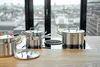 A set of stainless steel pots and pans on a kitchen countertop with a city view in the background. Produktbild-Vorschau