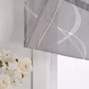 A close-up view of a grey roman blind with a white curved stripe pattern, partially drawn, with white flowers in the foreground. Produktbild-Vorschau