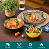 A table setting with colorful ceramic dishes filled with food, a glass of water, and a potted plant. Produktbild-Vorschau