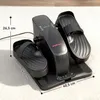 A black mini elliptical trainer is shown on a carpeted floor, with dimensions indicated by lines and text. Produktbild-Vorschau