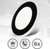 A close-up, angled view of a circular light fixture with a black outer ring and a white inner surface, set against a blurred white and gray background. Below the fixture are three circular icons with text and symbols. Produktbild-Vorschau