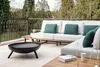 A modern outdoor patio with a sectional sofa, decorative pillows, and a black steel fire pit. Produktbild-Vorschau