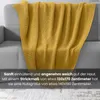 A yellow knitted blanket draped over a gray sofa. Náhľad obrázku produktu