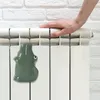A hand rests on a white radiator with a green ceramic crocodile humidifier attached. Produktbild-Vorschau