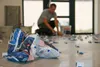 A person is kneeling on a floor, placing small blue leveling clips. Several bags of what appear to be tile leveling system components are in the foreground. Náhľad obrázku produktu