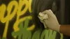 A gloved hand is wiping away spray paint from a surface with graffiti. Produktbild-Vorschau