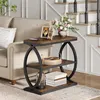 A narrow, three-tiered side table with a rustic brown wood finish and black metal frame, placed next to a sofa in a living room setting. Anteprima dell’immagine prodotto