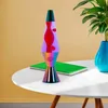 A lava lamp sits on a white table next to a green notebook and a blue vase with a plant. Podgląd zdjęcia produktu