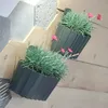Two dark gray planters with green plants and pink flowers are mounted on a wooden wall, with a textured gray surface in the background. Produktbild-Vorschau