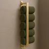 A gold-colored towel rack mounted on a tiled wall, holding several rolled green towels. Voir les images du produit