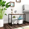 A small two-tier shelf unit with decorative items and books placed on it, next to a large potted plant. The shelf unit has a wood-look top and black metal frame. There are decorative items like a trophy and a small clock on the top shelf, books and a pen h Produktbild-Vorschau