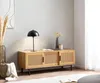 A living room scene featuring a wooden TV stand with cane detailing, a lamp, and decorative items. Produktbild-Vorschau