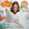A woman is wrapped in a white duvet, smiling. Produktbild-Vorschau
