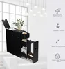 A black narrow storage cabinet with drawers and a door, placed next to a white sofa, with a window and hanging lights in the background. Náhľad obrázku produktu