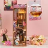 A miniature Japanese grocery store diorama, part of a DIY book nook kit, displayed on a pink background with decorative flowers and a small tree. Voir les images du produit