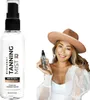 A woman in a hat holds a bottle of tanning mist next to a larger bottle of the same product. Produktbild-Vorschau