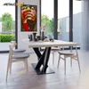 A dining table with a modern spider leg base, set in a well-lit room with large windows overlooking a garden. The table is set with decorative items. Náhled obrázku produktu