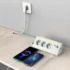 A white power strip with multiple outlets and USB ports is plugged into a wall socket and is charging two smartphones on a wooden desk. Produktbild-Vorschau