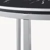 A close-up view of the edge of a round table with a black marble pattern and silver legs. Voir les images du produit