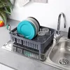 A dish rack filled with plates and glasses is placed on a countertop next to a sink and faucet. Produktbild-Vorschau