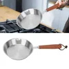 A person is holding a stainless steel frying pan with a wooden handle over a stovetop. Produktbild-Vorschau