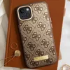 A Guess iPhone case is shown on top of a brown notebook, with jewelry nearby. Náhled obrázku produktu