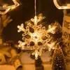 A close-up of a snowflake-shaped LED light hanging, with blurred Christmas trees in the background. Produktbild-Vorschau