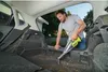 A man is vacuuming the trunk of a car with a handheld vacuum cleaner. Podgląd zdjęcia produktu
