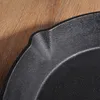 A close-up view of the edge of a black cast iron frying pan resting on a wooden surface. Produktbild-Vorschau