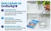 A hand holding a spoon over a glass of water, with a product package and instructions on the side. Produktbild-Vorschau