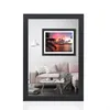 A framed picture of a sunset over the ocean with palm trees in the foreground, displayed in a living room setting with a pink sofa and a coffee table. Produktbild-Vorschau