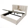 A beige upholstered bed frame with the mattress support mechanism partially raised, revealing the storage space underneath. The headboard has integrated cup holders and a small shelf. Anteprima dell’immagine prodotto