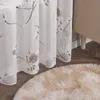 A close-up view of a sheer curtain with a floral pattern, a fluffy rug, and a piece of furniture. Produktbild-Vorschau
